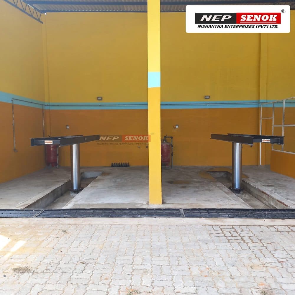 Two single-post washing lifts installed in a finished wash bay, platforms lowered over their in-ground pits.