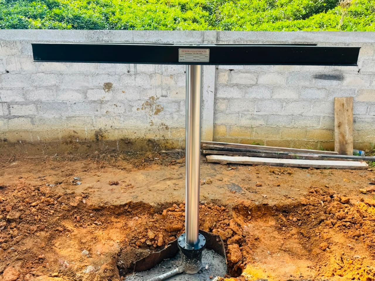 A washing lift column being set into an excavated pit on site, its platform beam bolted in place against a block wall.